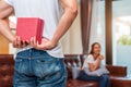 Man holding gift behind him for surprise girlfriend at their home. Woman waiting for Valentines gift form boyfriend. Happy