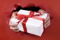 Man holding or giving a White Christmas gift with red ribbon through a red torn paper background