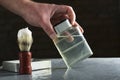 Man holding glass bottle of lotion after shave, brush with shave cream on the grey surface against dark brick wall