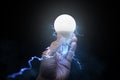 Man holding glowing light bulb with electricity and lightning bolts against black brackground Royalty Free Stock Photo