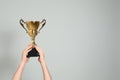 Man holding gold trophy cup on grey background, closeup. Space for text Royalty Free Stock Photo