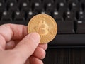 A man holding a golden bitcoin coin in his hand against a computer keyboard Royalty Free Stock Photo