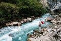 Man holding guitar standing on the bank of a mountain river on a background of rocks and forest. Handsome hippie style guitarist