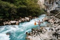 Man holding guitar standing on the bank of a mountain river on a background of rocks and forest. Handsome hippie style guitarist