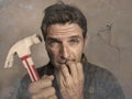 Man holding hammer driving a nail for hanging a frame but making funny faces for the mess cracking the wall as a disaster DIY guy