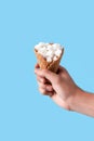 Man holding in hand ice-cream wafer cone filled with white sugar cubes isolated on blue background Royalty Free Stock Photo