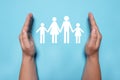 Man holding hands around paper silhouette of family on light blue background, top view. Insurance concept Royalty Free Stock Photo