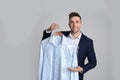 Man holding hanger with shirt in plastic bag on grey background. Dry-cleaning service Royalty Free Stock Photo