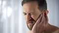 Man holding his aching ear, suffering from otitis, sudden hearing loss, close up