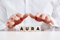 Man holding his hands protectively over the wooden cubes with the word aura