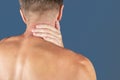 Man holding his neck in pain, isolated on blue background. Lower neck pain. Shirtless man touching his neck for the pain