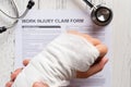 Man holding his wrapped hand on top of a work injury claim form with stethoscope medical & insurance concept