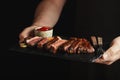 Man holding juicy grilled beef steak with spices and red sauce on a stone cutting board on a black background Royalty Free Stock Photo