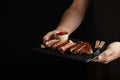 Man holding juicy grilled beef steak with spices and red sauce on a stone cutting board on a black background. With copy space for Royalty Free Stock Photo