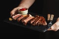 Man holding juicy grilled beef steak with spices and red sauce on a stone cutting board on a black background Royalty Free Stock Photo