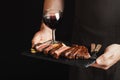 Man holding juicy grilled beef steak with spices and red wine glass on a stone cutting board on a black background. With Royalty Free Stock Photo