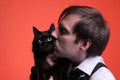 Man holding and kissing on muzzle black cat on orange background