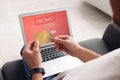 Man holding laptop with activated promo code and credit card on sofa, closeup