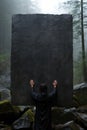 A man props up a large stone in the woods, AI