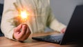 Man holding a light bulb while working on a computer laptop to think and generate new ideas through technological innovation. Royalty Free Stock Photo