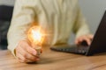 Man holding a light bulb while working on a computer laptop to think and generate new ideas. Royalty Free Stock Photo
