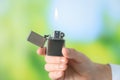 Man holding lighter with burning flame against blurred green background, closeup Royalty Free Stock Photo