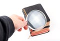 Man holding a loupe, magnifying glass in hand inspecting small old antique books, taking a closer look