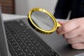 Man holding magnifier near laptop at table, closeup. Online searching concept