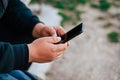 Man holding mobile phone outdoor. Traveler with black hoodie using smarphone sitting outside. photo from aside Royalty Free Stock Photo