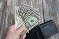 Man is holding money in hand. The black leather wallet lying on rustic wooden background. Dollars for making purchases and byung Royalty Free Stock Photo