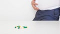 The man is holding onto a fat stomach, in front of him are pills on the table for weight loss. Medications to reduce bloating and