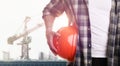 Man holding orange hat at construction site with unfinished building, closeup. Space for text Royalty Free Stock Photo