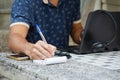 Man holding pen writing notes in notebook paper while meeting online Royalty Free Stock Photo