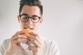Man holding a piece of hamburger. student eats fast food. not helpful food. very hungry man. Nerd is wearing glasses. Royalty Free Stock Photo