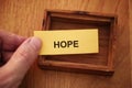 A man holding a piece of yellow paper with the word Hope on it in his hand over a small empty wooden box. Royalty Free Stock Photo