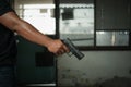 Man holding a pistol, standing in a room in black, pointing and aiming a gun at a target. concept of assassination, murder, Royalty Free Stock Photo