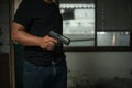 Man holding a pistol, standing in a room in black, pointing and aiming a gun at a target. concept of assassination, murder, Royalty Free Stock Photo