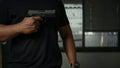 Man holding a pistol, standing in a room in black, pointing and aiming a gun at a target. concept of assassination, murder, Royalty Free Stock Photo