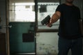 Man holding a pistol, standing in a room in black, pointing and aiming a gun at a target. concept of assassination, murder, Royalty Free Stock Photo