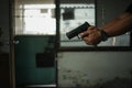 Man holding a pistol, standing in a room in black, pointing and aiming a gun at a target. concept of assassination, murder, Royalty Free Stock Photo