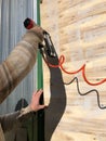 A man is holding a pneumatic nail gun and attaching plywood to the frame of the house.