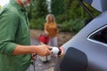 Man holding power supply cable, while his wife waiting for car charging at electric vehicle charging station, closeup Royalty Free Stock Photo