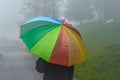 Man holding rainbow colored umbrella going down a street on foggy rainy day in autumn Royalty Free Stock Photo