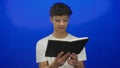 Man holding and reading open black book with visible pages in blue studio; curiosity learning focus education Royalty Free Stock Photo