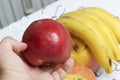 The man is holding a red apple in his hand. There is a fruit basket in the background. Several apples and bananas.