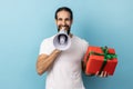 Man holding red present box and screaming in megaphone, making announcement. Royalty Free Stock Photo