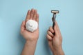 Man holding shaving foam and razor on light blue background, top view