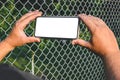 A man is holding a smartphone mockup in his hands. Against the background of a steel wire fence and nature. Close-up view Royalty Free Stock Photo