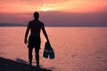 Man holding snorkel fins on beach at sunset Royalty Free Stock Photo