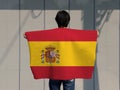 The man holding Spain flag on his shoulder and turn back on grey background
